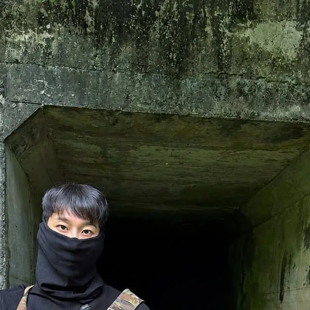 이끼 낀 콘크리트 굴 입구 앞에서 검은 복면을 쓴 사람